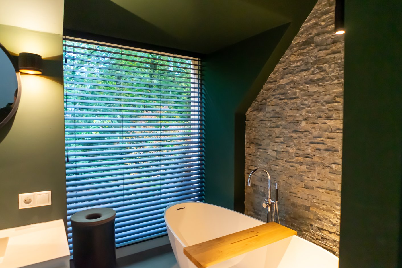 Houten jaloezieën in een luxe badkamer met groene muur