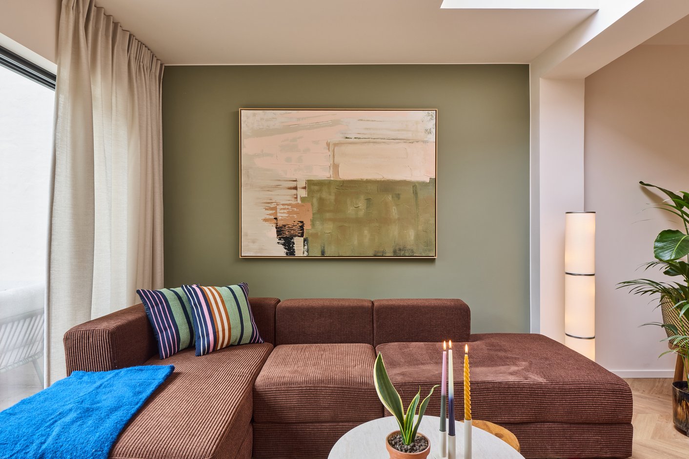 Woonkamer met groene muur, bruine bank en witte gordijnen