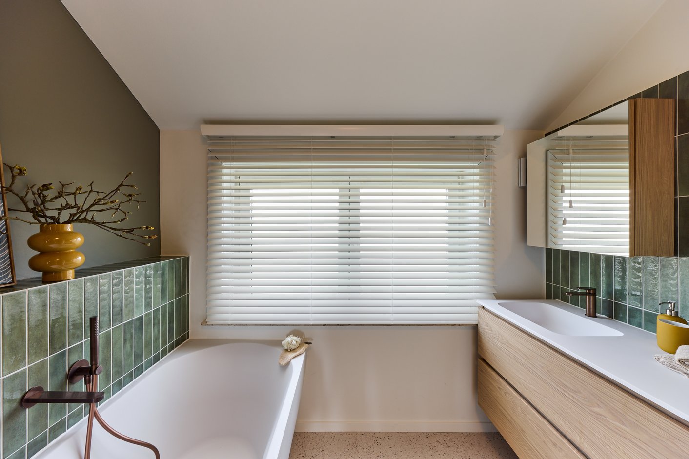 Badkamer met groene tegels en witte houten jaloezieën